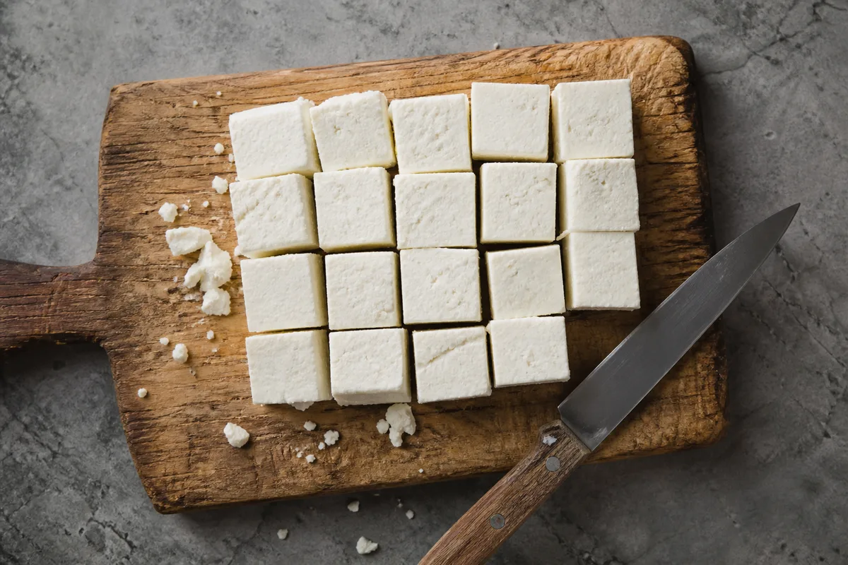 Cubes de paneer frais posés sur une planche en bois, texture ferme et blanche